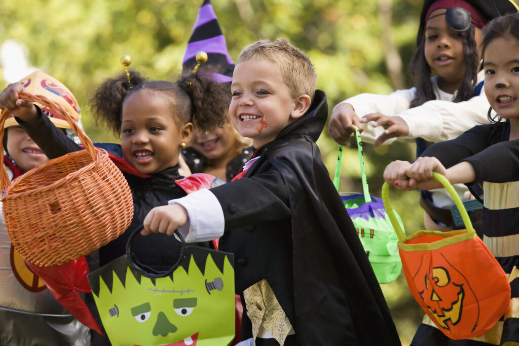 Little children wearing costumes trick-or-treating on Halloween.