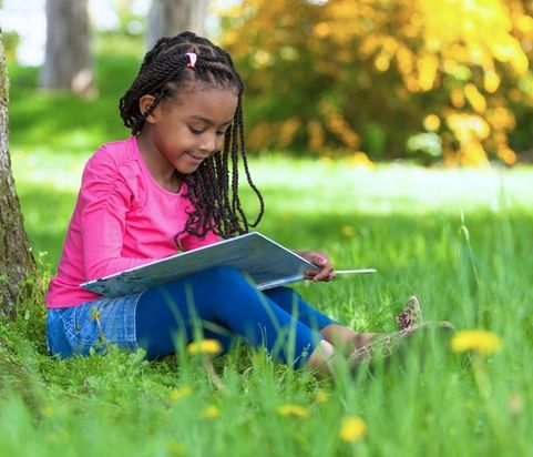Early elementary aged girl sitting on lawn reading a book