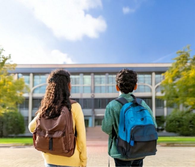 two elementary aged kids wearing backpacks and walking into school