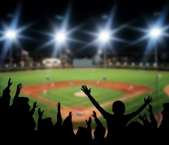 Silhouette of a crowd cheering at a baseball game with the field in the back.