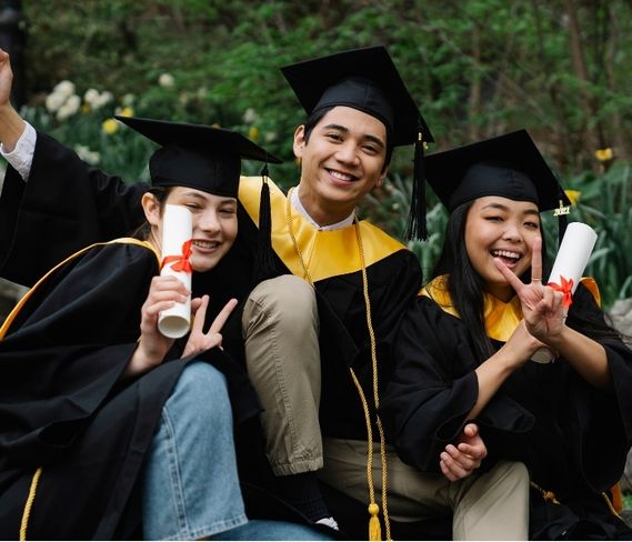 three students holding diplomas and wearing graduation caps